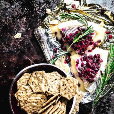 Gluten free baked brie on the table with fresh rosemary and pomegranate syrup.