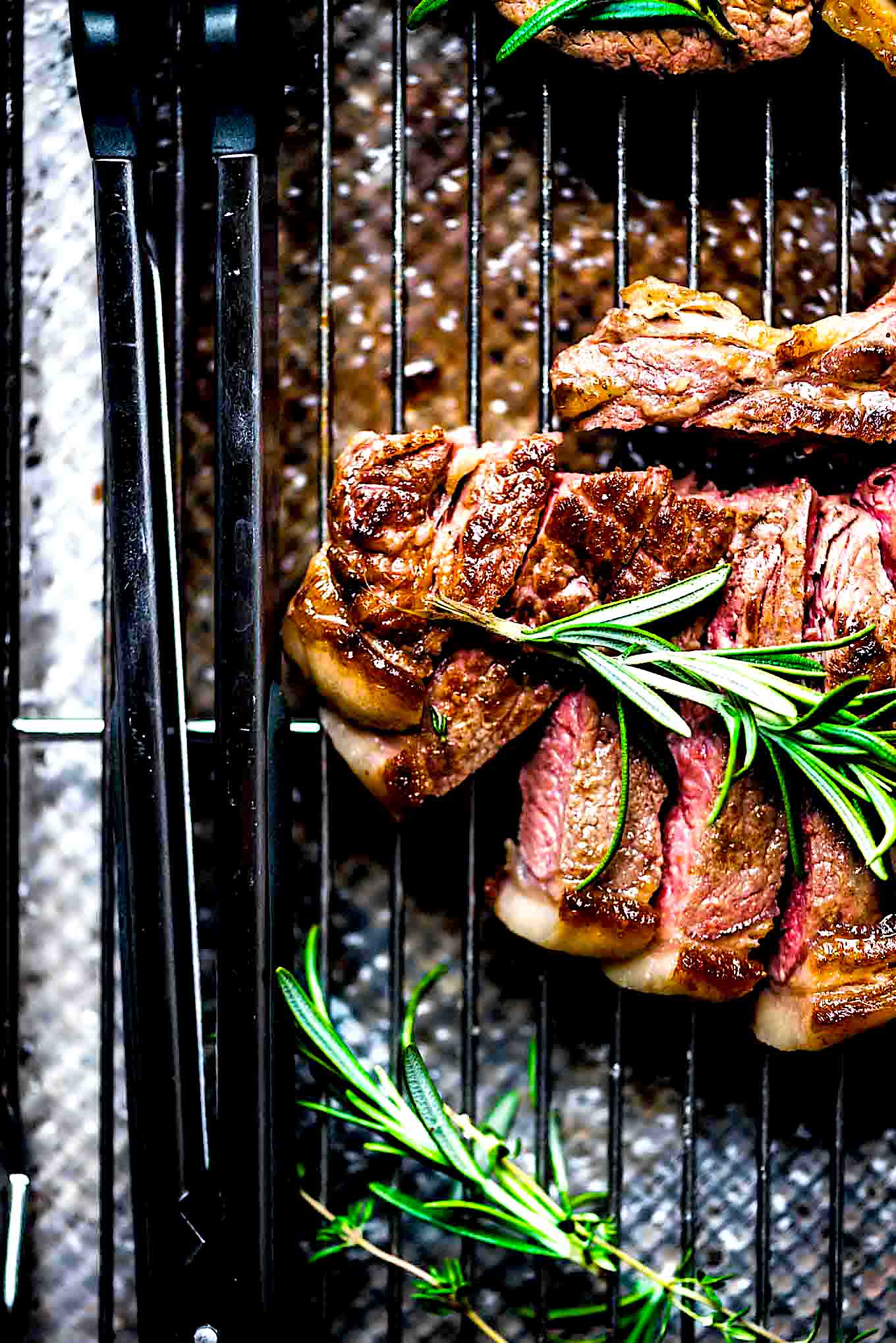 A sliced t-bone steak on a grill pan topped with a piece of rosemary.