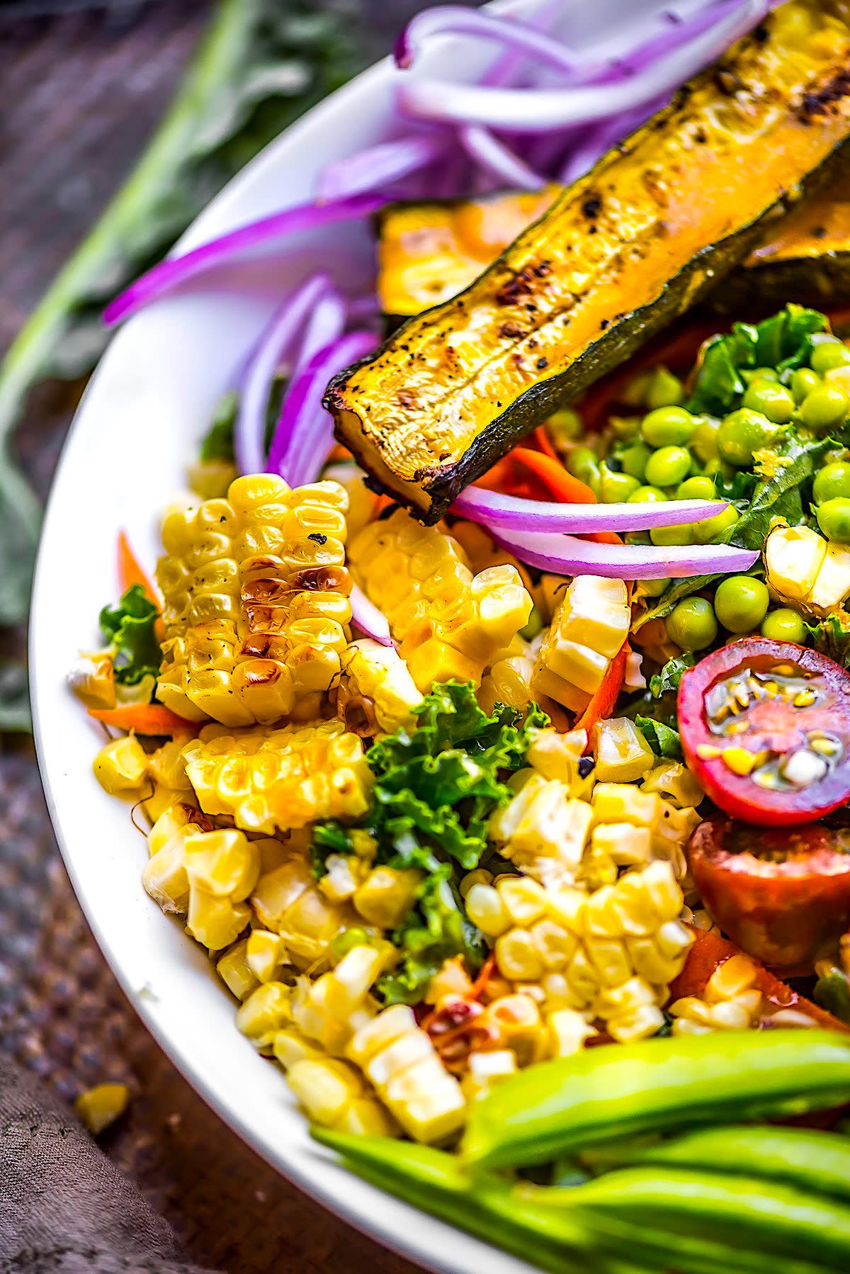 Zucchini corn salad in a bowl with onions, tomatoes, and snap peas in the bowl too.