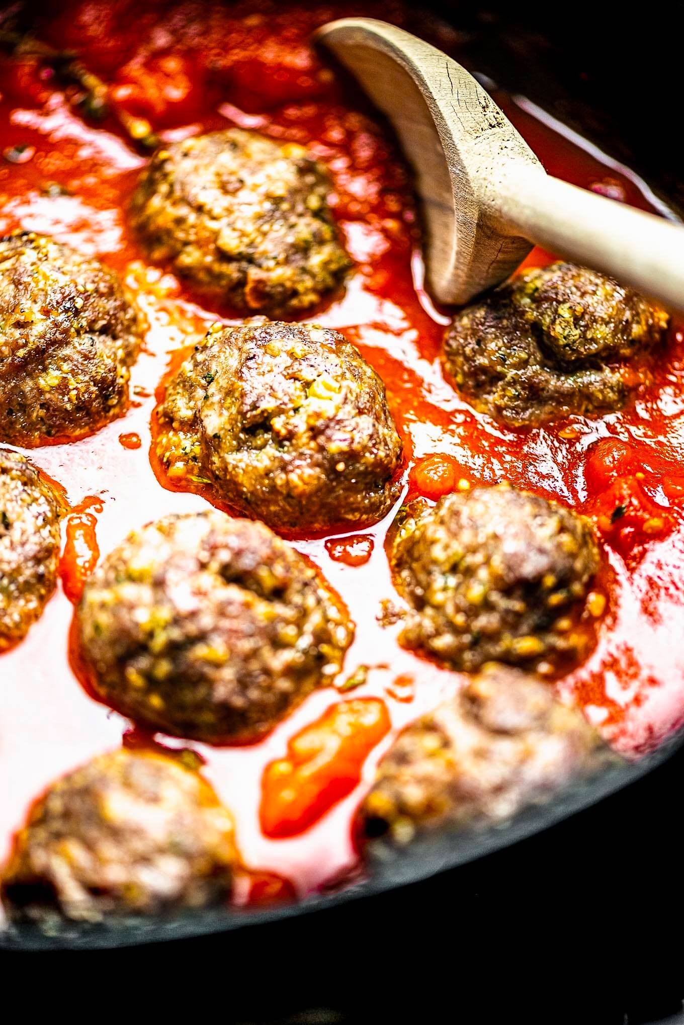 The meatballs added to the skillet with the tomato sauce and a wooden spoon in the pan.