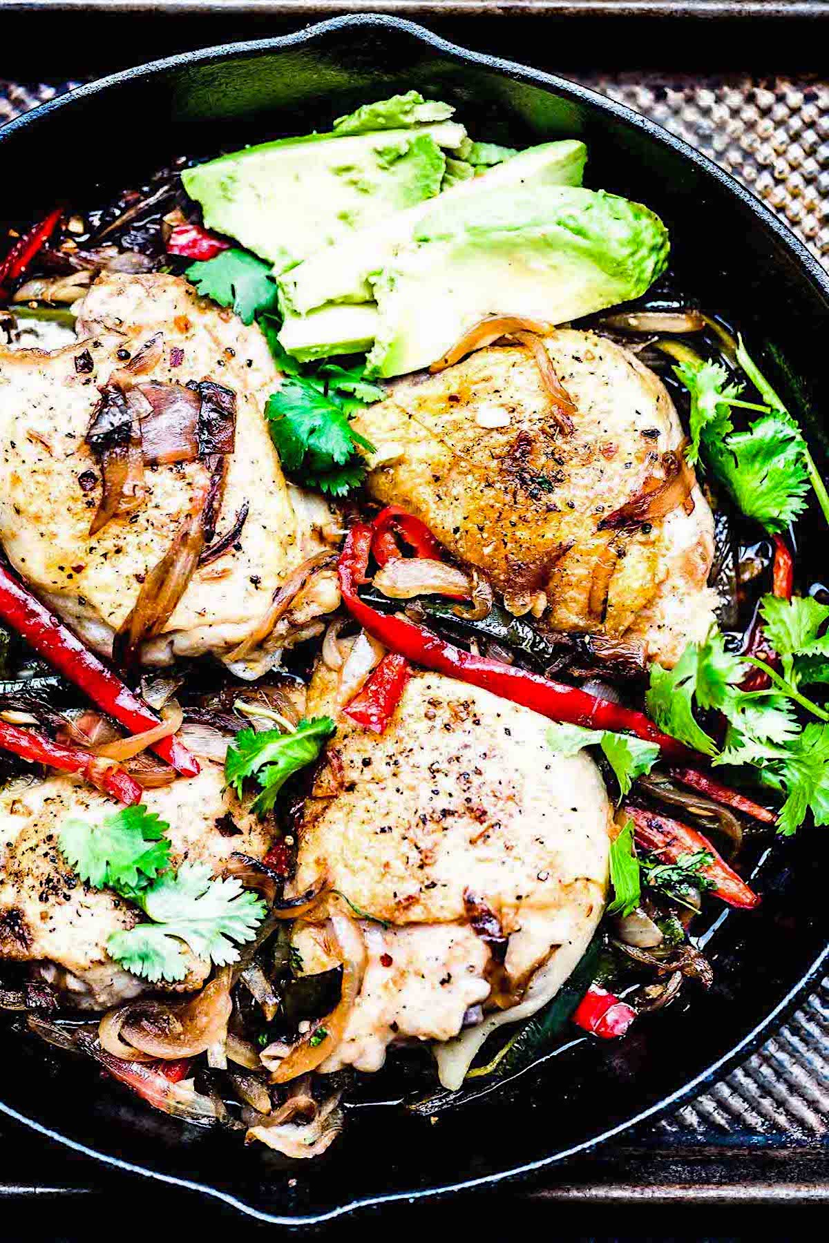 Skillet chicken thighs with poblanos garnished with fresh cilantro leaves in a skillet.