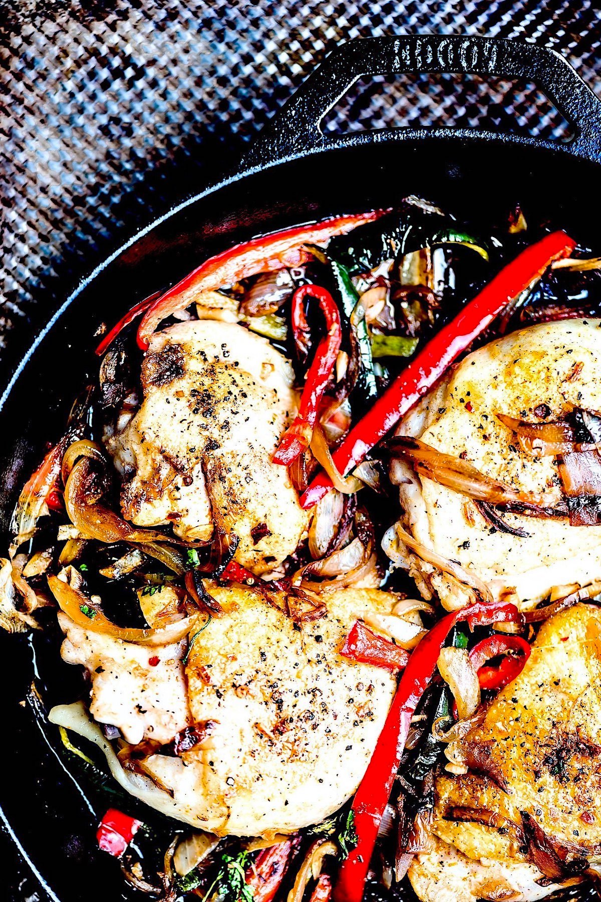 A skillet with chicken thighs and cooked peppers.