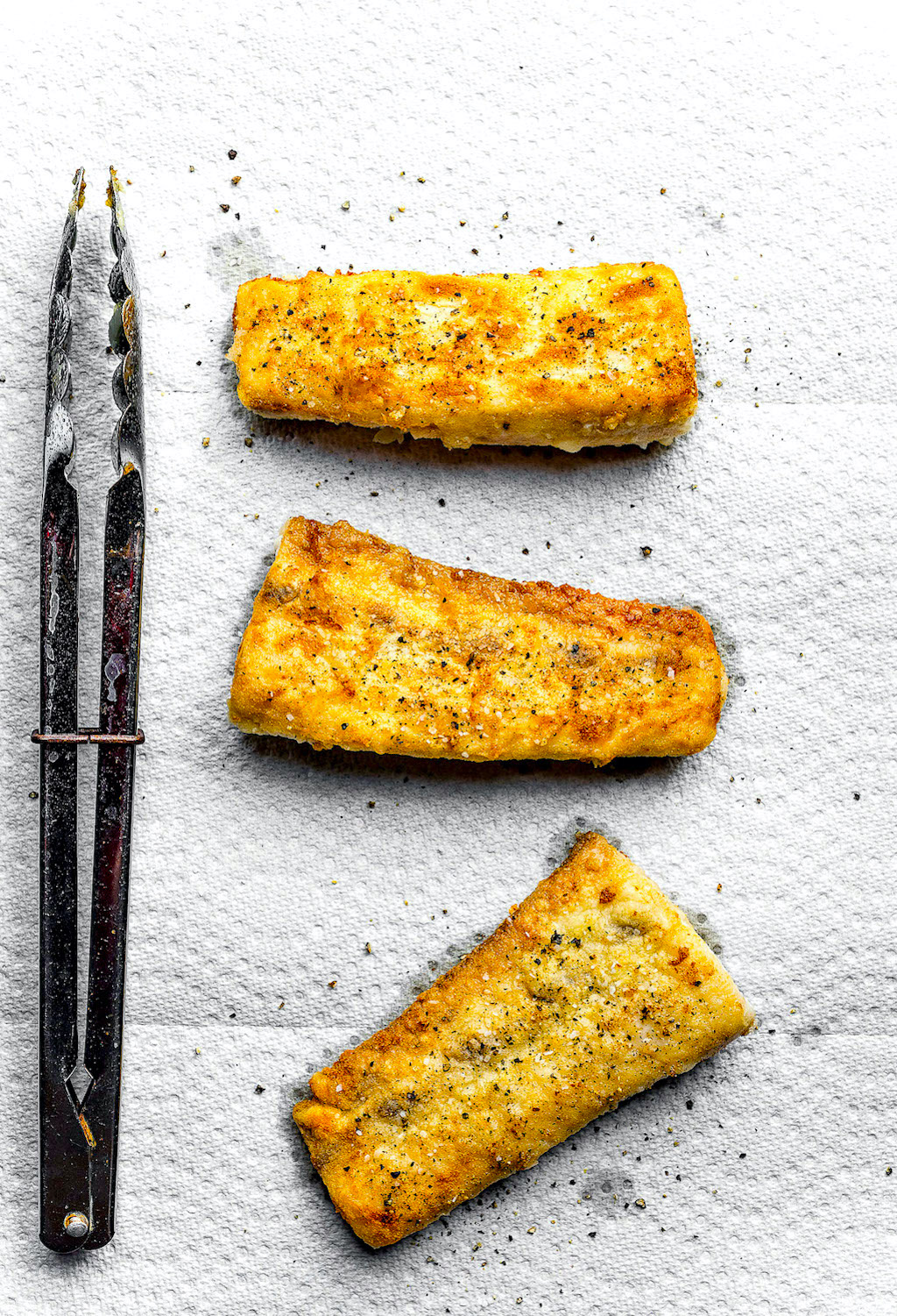 Gluten free fried Mahi-Mahi tuna lined on paper towels with tongs on side.