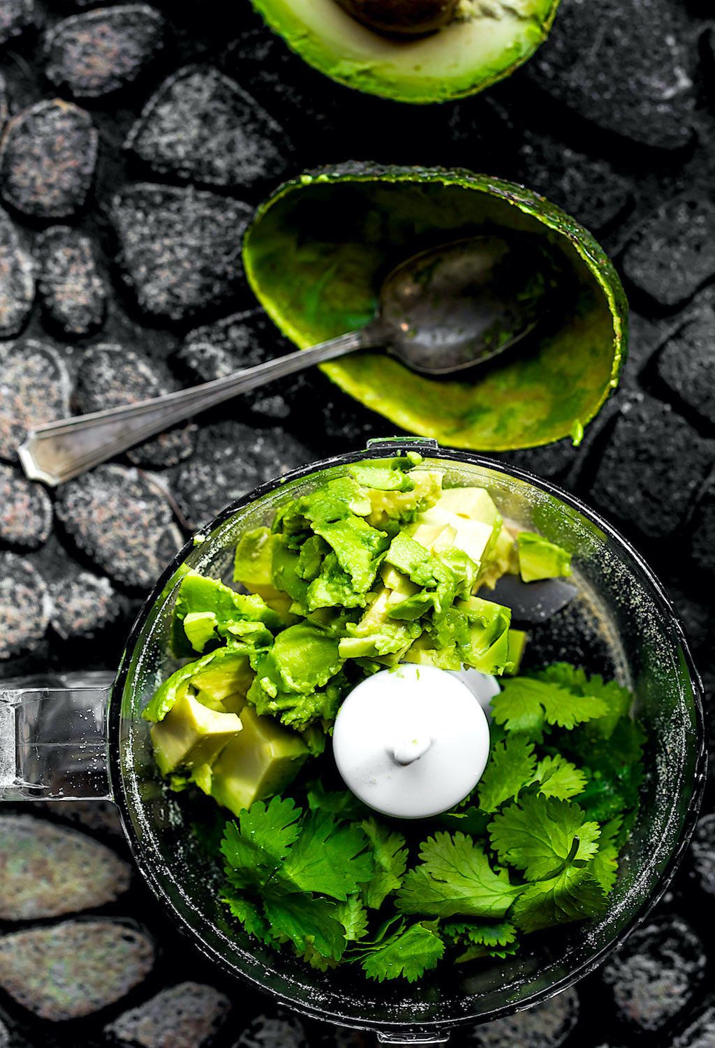 Avocado sauce in mini food processor with cilantro and spoon overhead shot.